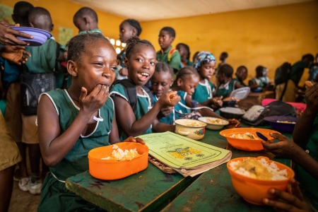 Kadiatu is eating a hot meal of rice and vegetables provided by the WFP supported school feeding program.